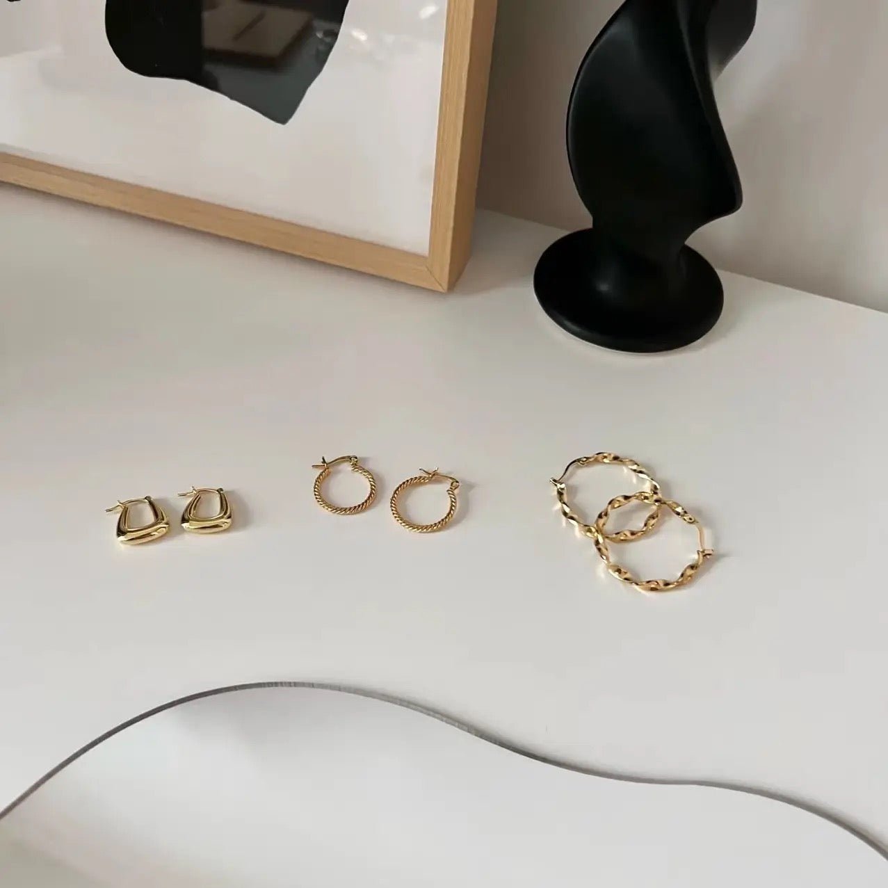 Collection of gold hoop earrings, including 18k gold vermeil twisted design, displayed on a stylish white surface.